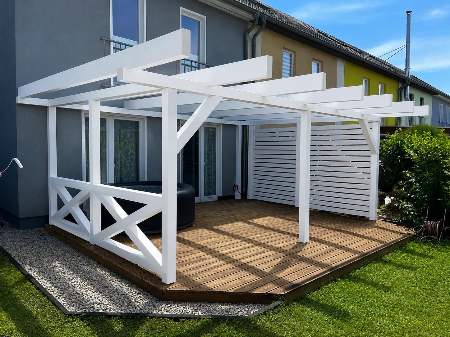 Weiß lackierte Holz-Pergola mit Lattenwand als Sichtschutz über einer Holzterrasse am Haus