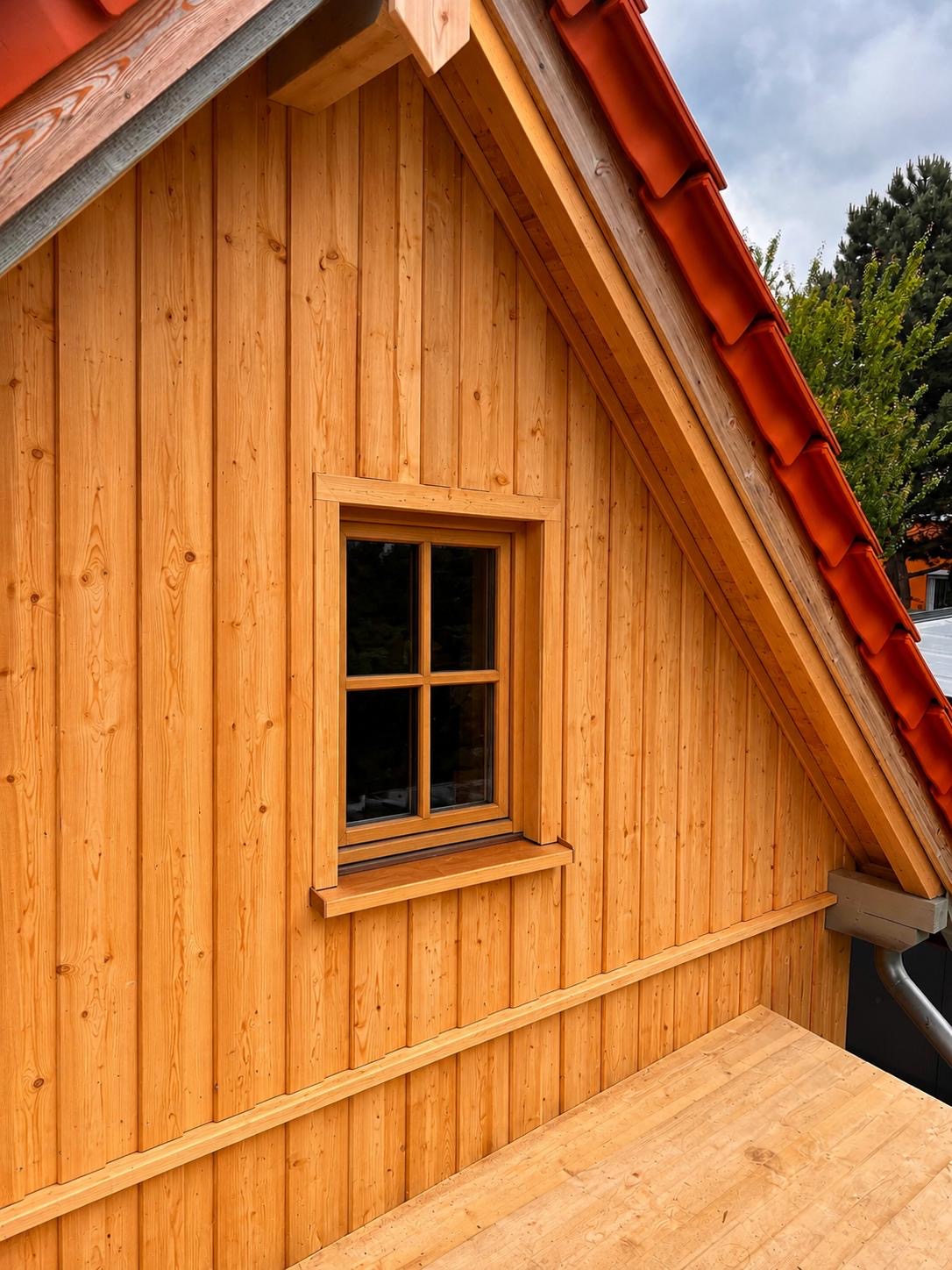 Holzfassade mit sichtbarer Vertäfelung an einem Giebel mit rotem Ziegeldach