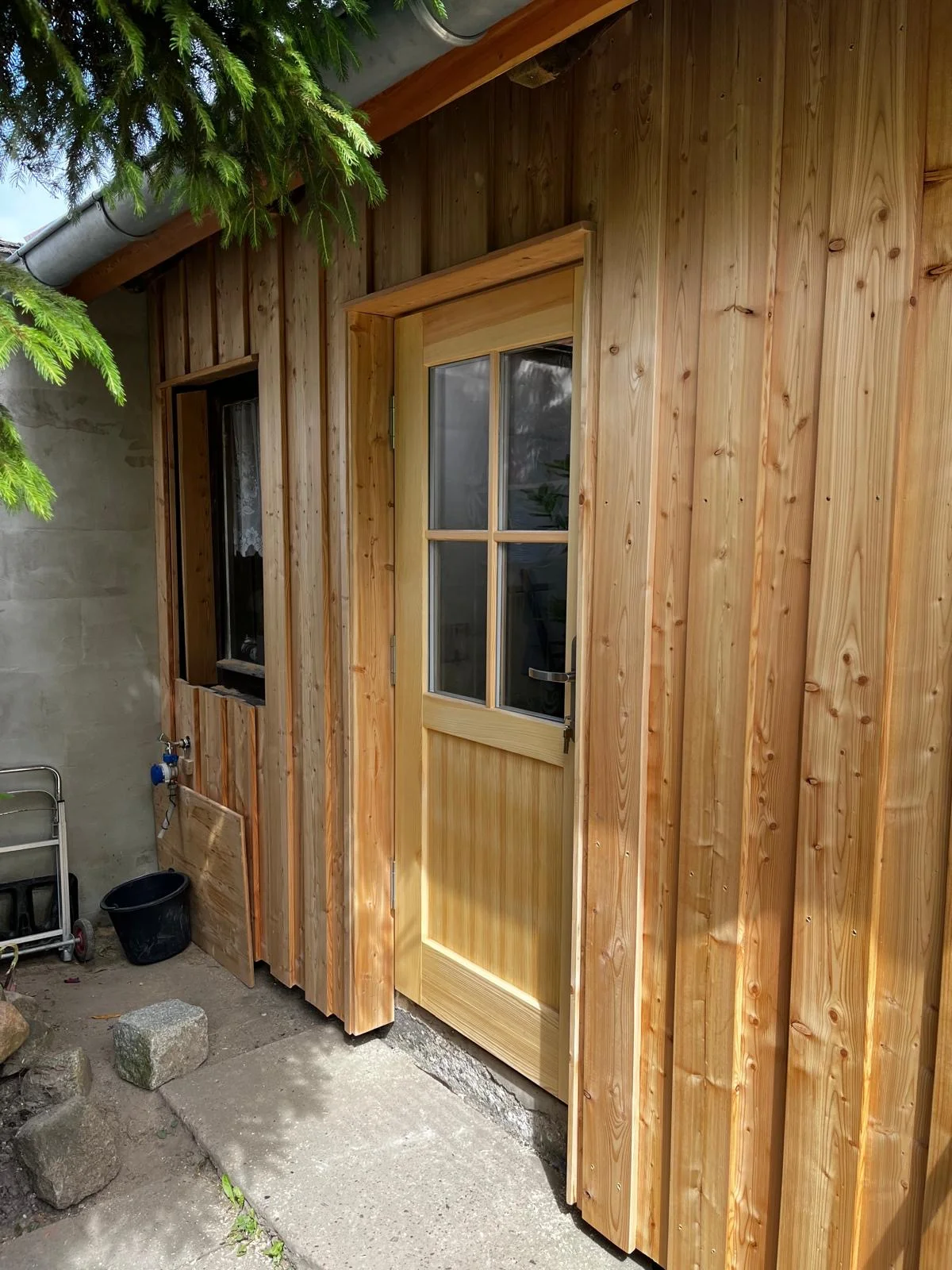 Neu eingebaute Holztür mit verglastem Oberteil in einer Holzfassade